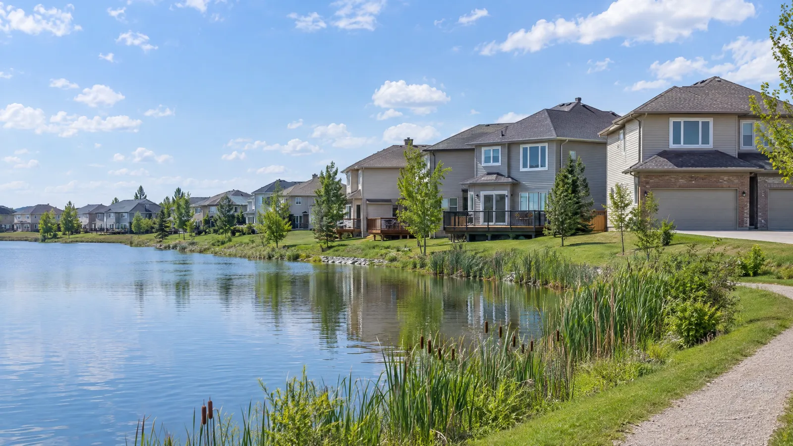 1990s two-storey suburban homes with casement windows and patio doors facing a pond in summer