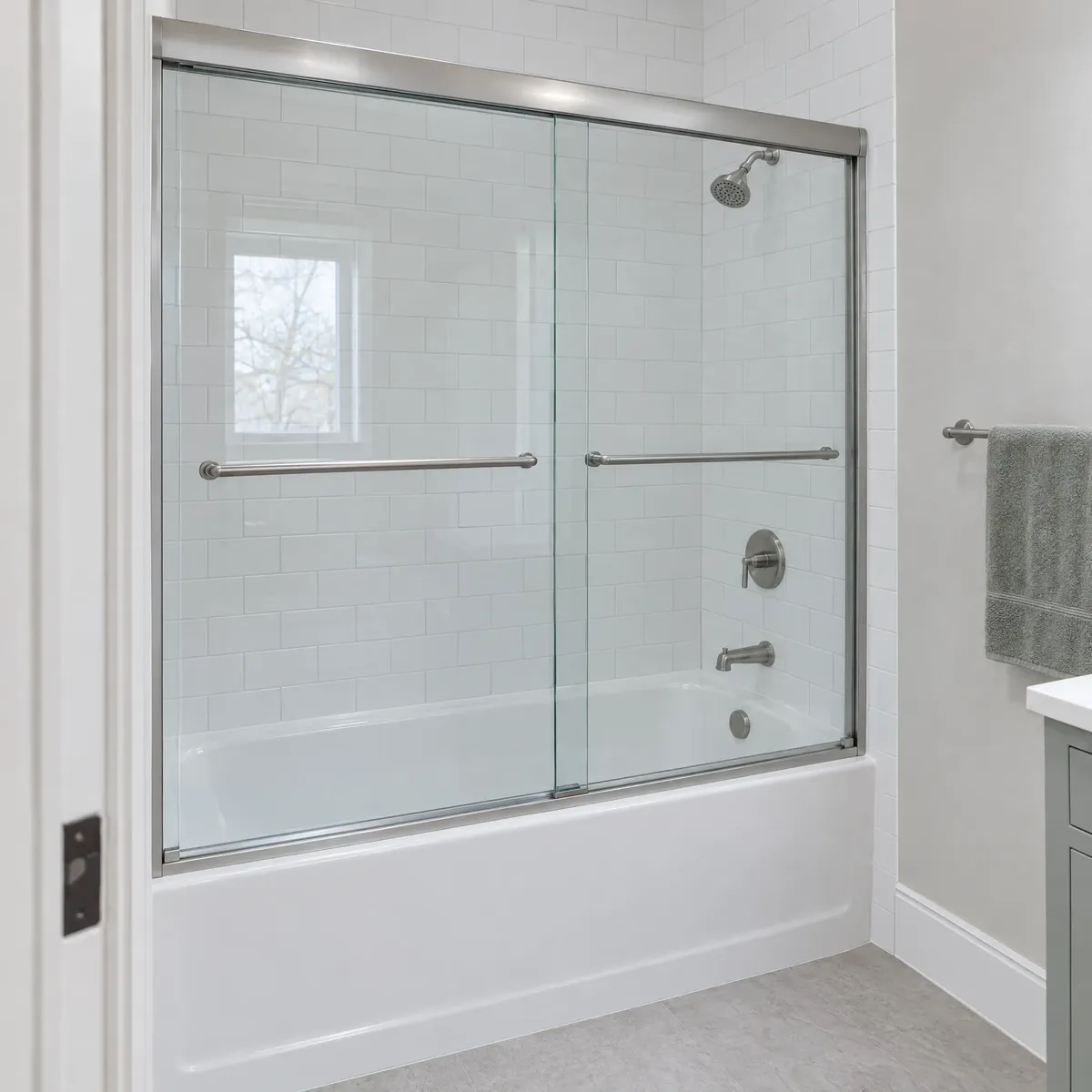 White bathtub with sliding glass tub doors in a subway-tile alcove